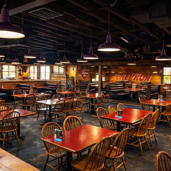 Spacious restaurant interior with red tables, wooden chairs, booth seating, and a large Chevron sign.