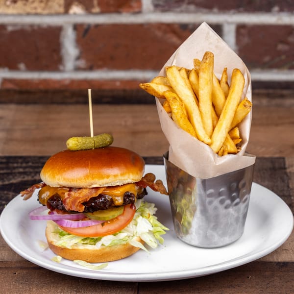 Bacon cheeseburger with lettuce, tomato, onion, and pickle, served with a side of fries.