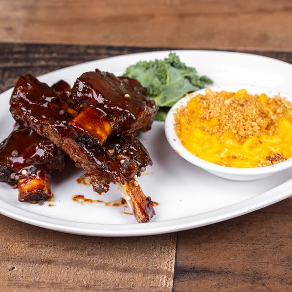 Glazed short ribs with mac and cheese and kale on a white plate.