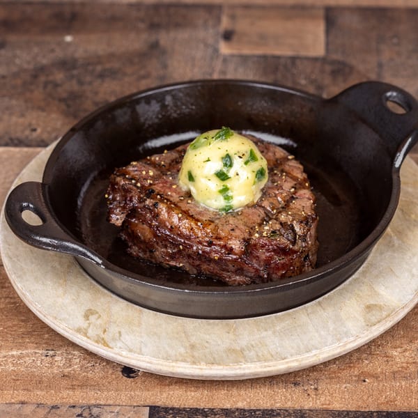 Grilled steak with a dollop of melting herb butter in a cast iron skillet on a wooden table.
