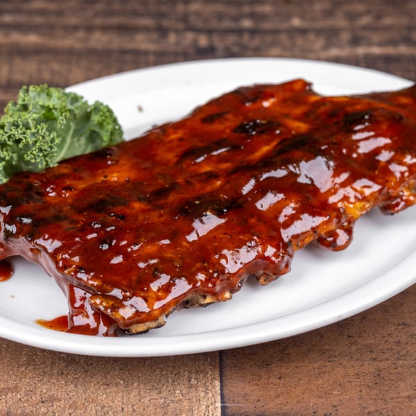 Original Roadhouse Grill's BBQ ribs, glistening with sauce, served on a white plate with a side of kale.