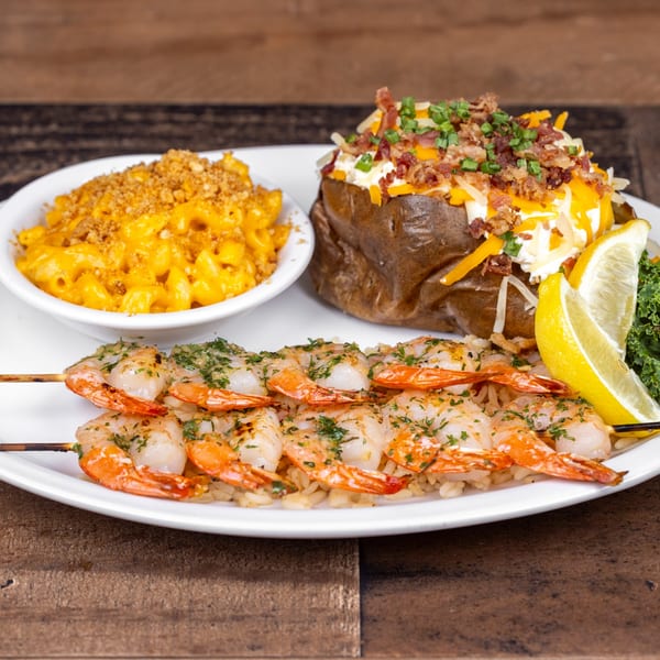 Grilled shrimp skewers on rice, with a loaded baked potato and mac and cheese.