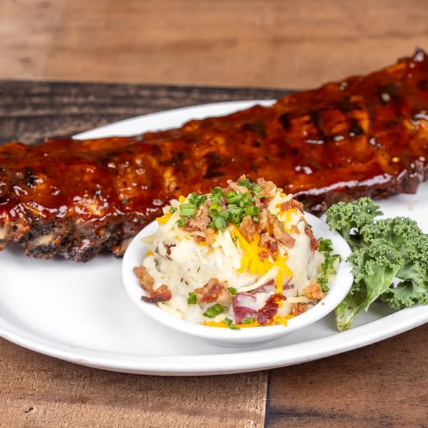 BBQ ribs with mashed potatoes topped with cheese, bacon, and chives, and a side of kale.