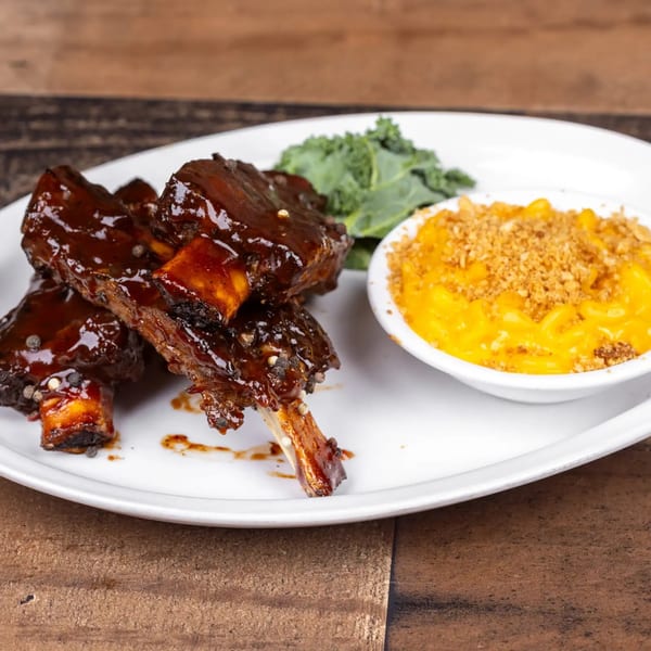 Glazed short ribs with black peppercorns, a side of mac and cheese, and kale on a white plate.