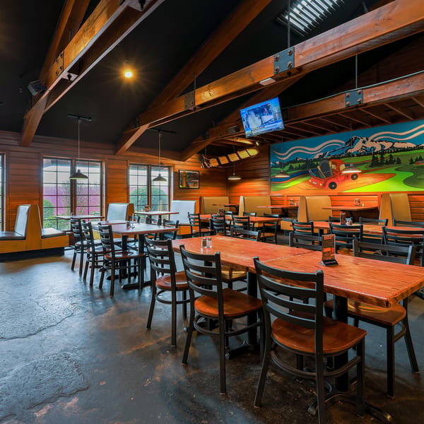 Spacious restaurant interior with wooden walls, exposed beams, booths, tables, chairs, and a colorful mural.
