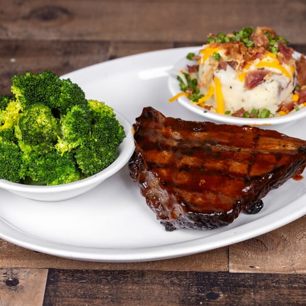 Original Roadhouse Grill's BBQ ribs, loaded mashed potatoes, and a side of broccoli on a white plate.