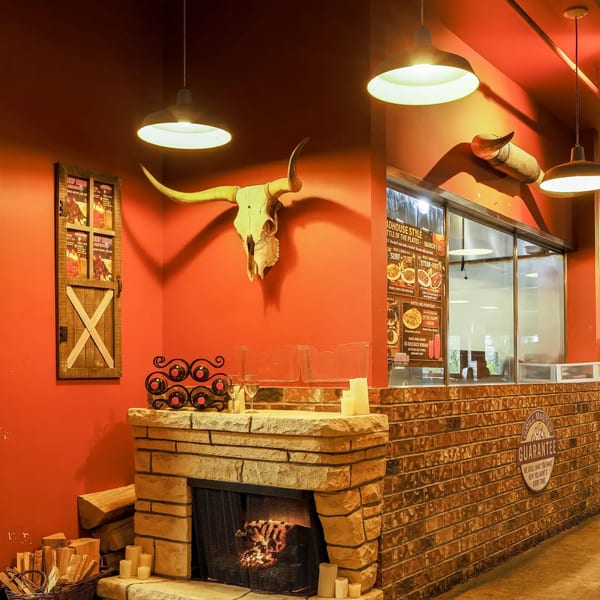 Original Roadhouse Grill interior with a stone fireplace, bull skull, and menu displays on a red wall.