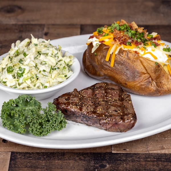 Original Roadhouse Grill steak dinner with baked potato, coleslaw, and kale on a white plate.