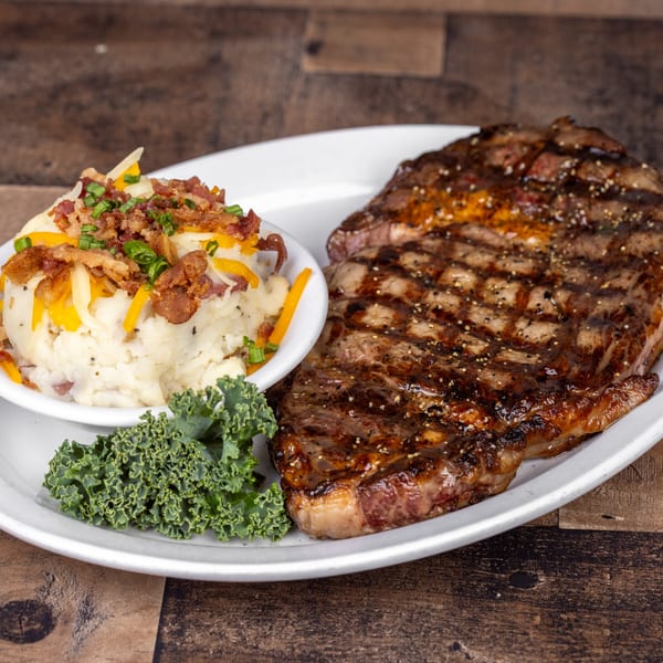 Grilled steak with mashed potatoes topped with cheese, bacon, and chives, and a side of kale.