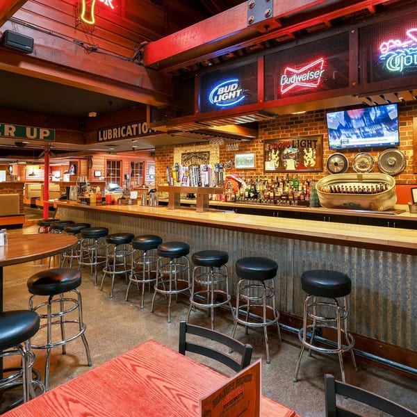 Original Roadhouse Grill's bar area with stools, neon signs, and a TV showing sports.