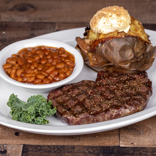 Original Roadhouse Grill steak dinner with baked potato, baked beans, and kale on a white plate.